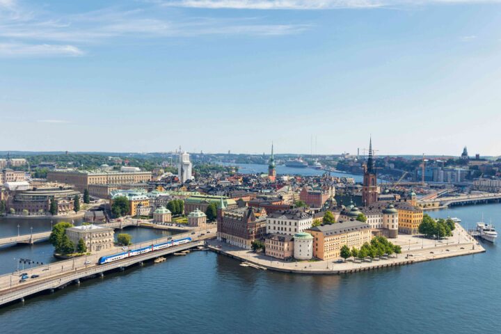 Flygbild av Stockholm med vatten och historiska byggnader under en klarblå himmel.