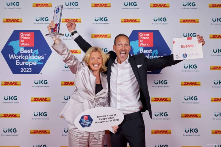 Två glada personer poserar med skylt och diplom framför en skylt med texten "Great Place to Work. Best Workplaces Europe 2023".
