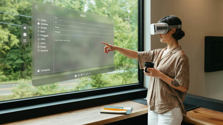 Kvinna med VR-glasögon interagerar med holografiskt e-postgränssnitt och håller en kopp.