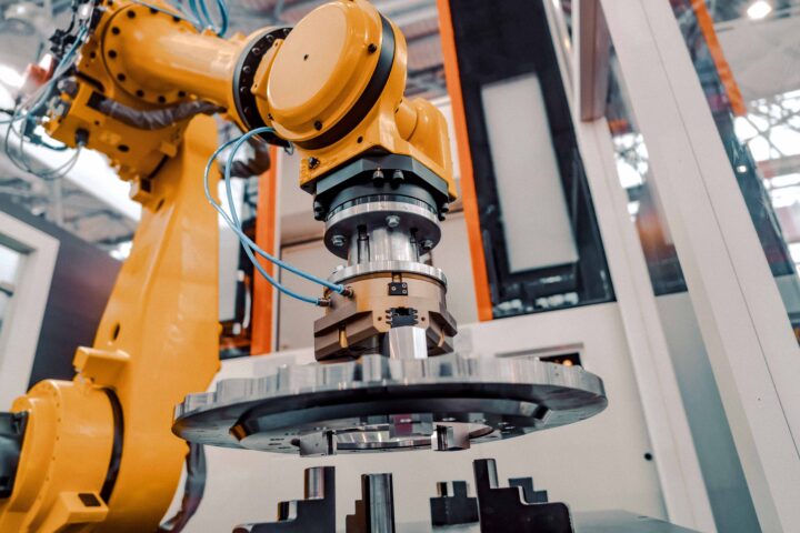 Gul robotarm monterar metallkomponent i fabriksmiljö.