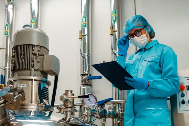 Worker in blue protective gear with clipboard in industrial setting.