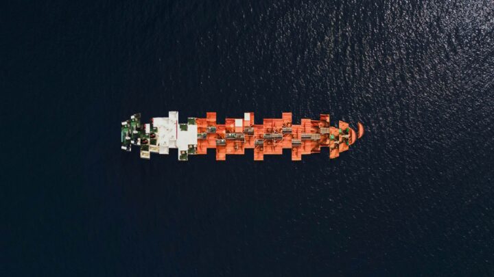 Fartyg ovanifrån i mörkt vatten, staplade containrar i rött och grönt på däck.