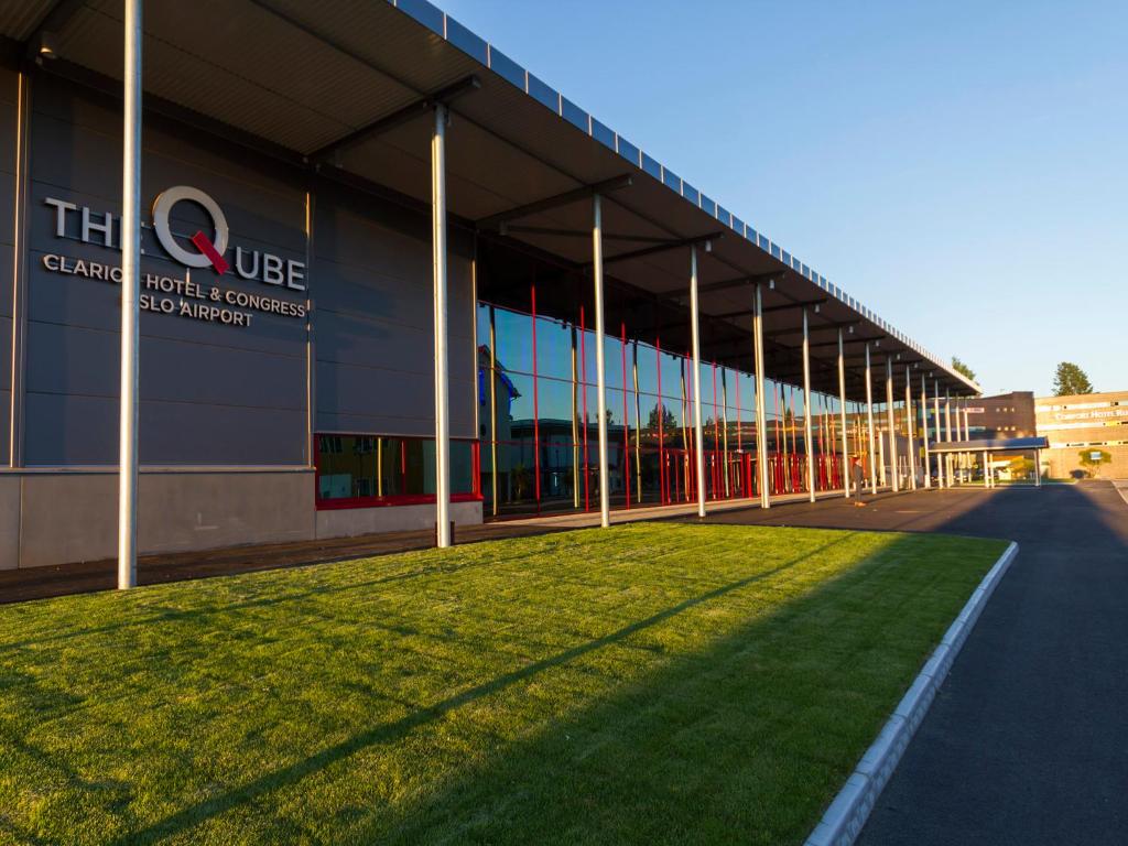 Modern byggnad med glasfasad och skylt "The Qube Clarion Hotel & Congress Oslo Airport", gräsmatta i förgrunden.