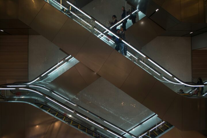 People ride modern, crossing escalators with metal panels and reflective lights in a dimly lit building interior.